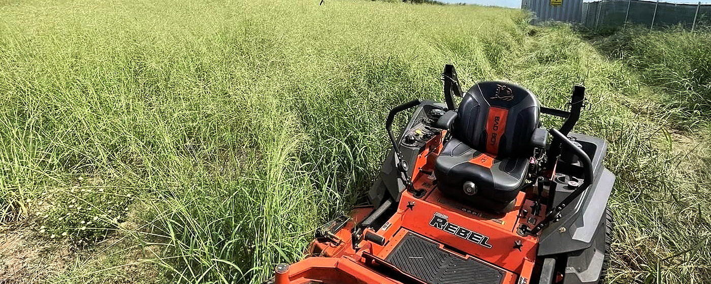 A Lipham Landscaping zero-turn mower cutting a path through an overgrown field